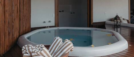 A wooden deck with a hot tub, a wicker basket with towels, and a door leading to a room.