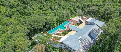 Vue aérienne d’un complexe hôtelier doté d’une piscine, de panneaux solaires et d’une végétation luxuriante qui entoure les bâtiments.
