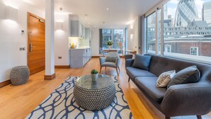 A modern living room with a sofa, a coffee table, and a view of a cityscape. - Tower Hill City Centre Luxury Apartments (London)