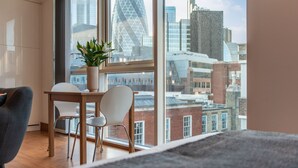 A modern room with a large window, a wooden table, two chairs, and a potted plant. - Tower Hill City Centre Luxury Apartments (London)