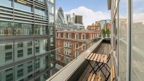 A modern building with large windows and a balcony with wooden seating. - Tower Hill City Centre Luxury Apartments (London)