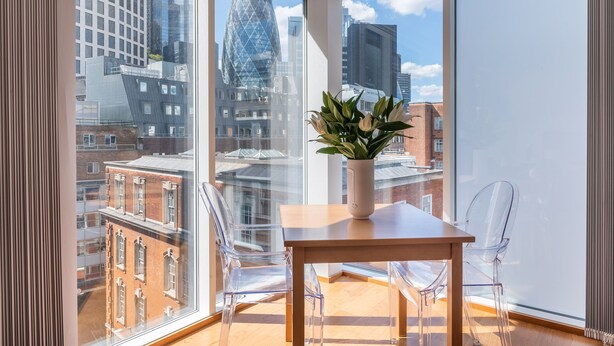 A modern room with large windows, a wooden table, and clear chairs. - Tower Hill City Centre Luxury Apartments (London)