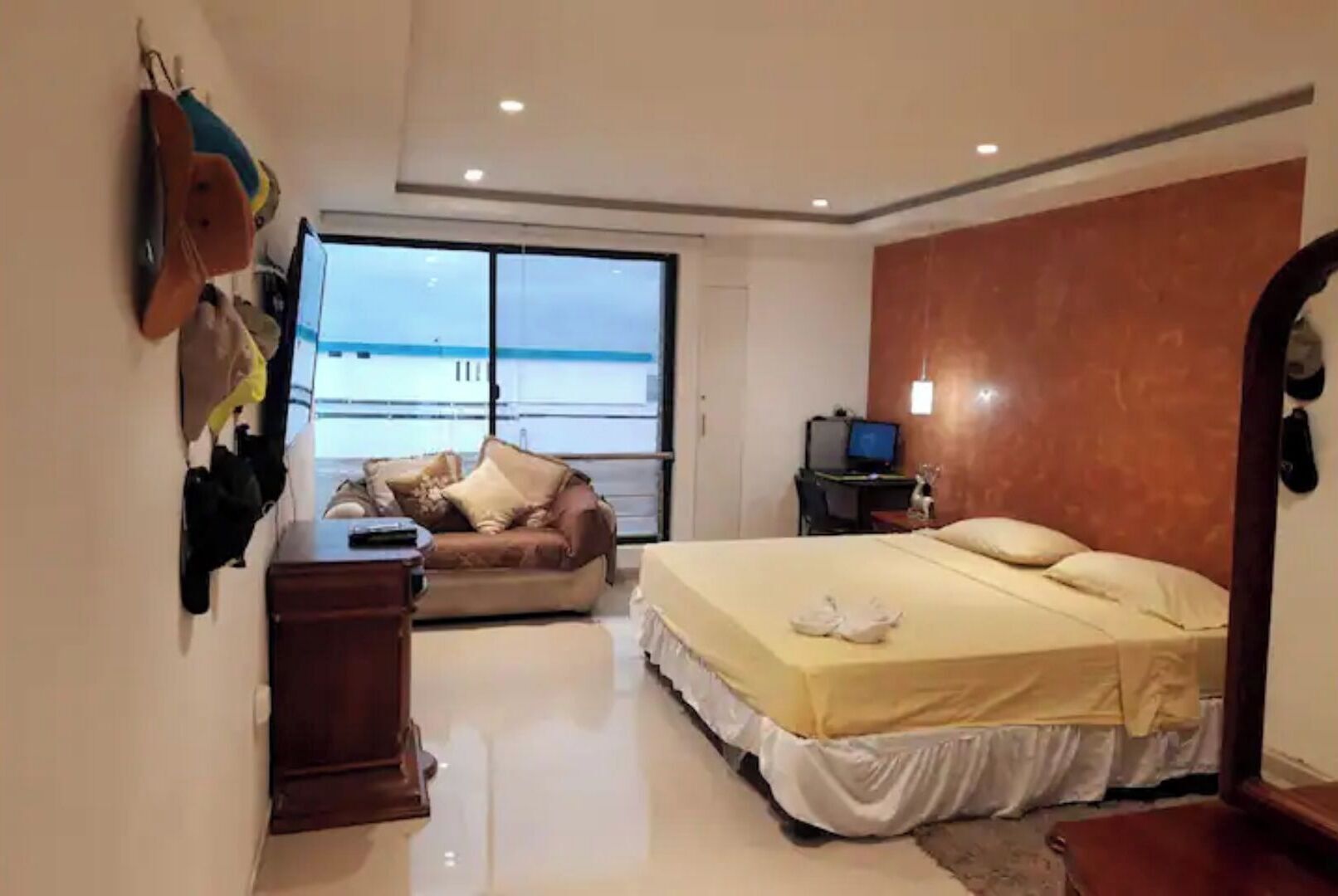 Een slaapkamer met een bed, een bureau, een stoel, een bank en een groot raam.