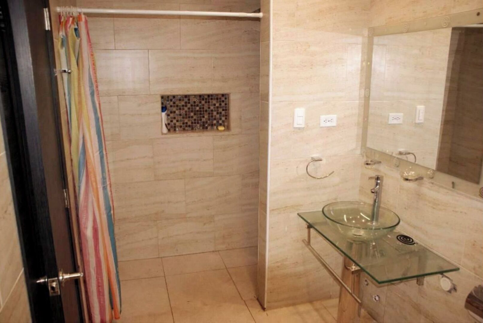A bathroom with a glass sink, a shower area, and a tiled wall.