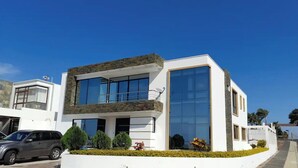 Una casa moderna de dos pisos con balcón, ventanas grandes y fachada blanca.