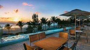 Un complexe hôtelier en bord de mer, doté d’une piscine, de meubles en bois et offrant une vue sur le coucher de soleil.