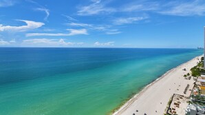 Une plage côtière aux eaux turquoise et limpides, avec un rivage sablonneux et un immeuble de grande hauteur sur la droite.