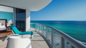 Un balcon avec vue sur l’océan, un lit et un coin salon avec des coussins.