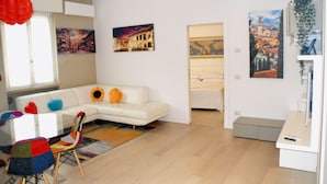 Ein modernes Wohnzimmer mit einem weißen Sofa, bunten Stühlen, einem Glastisch und Kunstwerken an den Wänden.