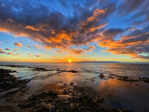 A sunset over a rocky shoreline with the sun reflecting off the water.