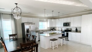 A modern kitchen with white cabinets, a central island, stainless steel appliances, and a dining area with wooden chairs. - Rip Line Lodge at Venice Marina- 3bedroom/2bath lodge (Venice)