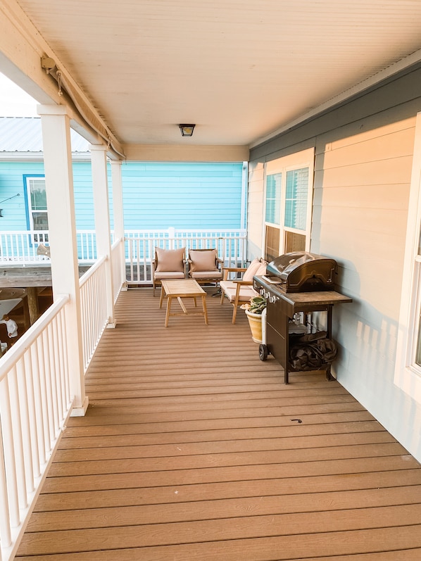 A wooden porch with a railing, two chairs, a table, and a grill.
