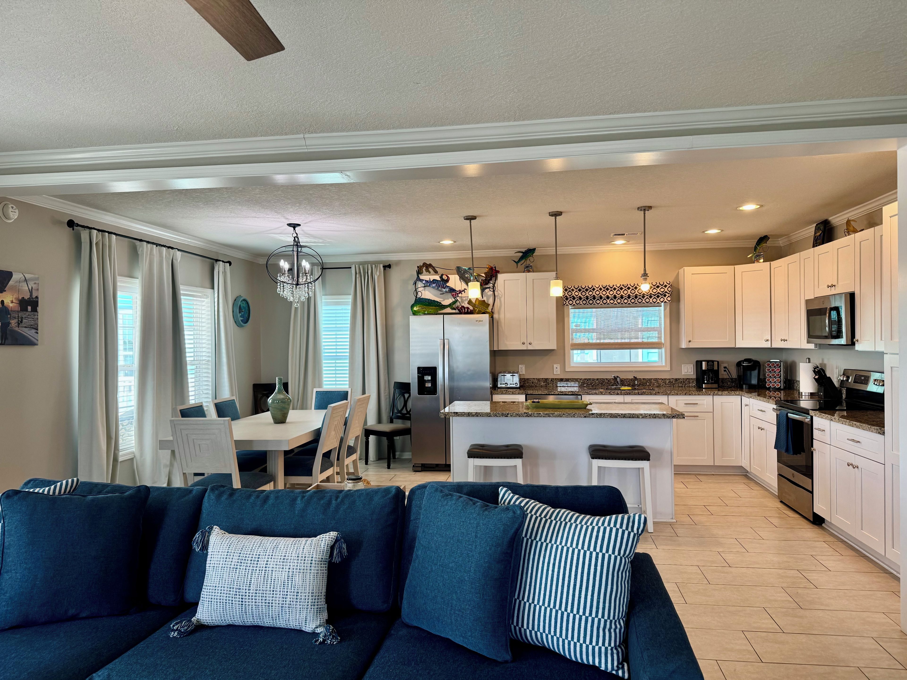 A modern living room with a dark blue sofa, a dining area with a white table, and a kitchen with white cabinets and stainless steel appliances.