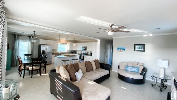 A modern living room with a sectional sofa, a dining area with a table and chairs, and a kitchen in the background. - Rip Line Lodge at Venice Marina- 3bedroom/2bath lodge (Venice)