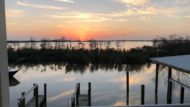 A waterfront view with a dock and a pier extending into calm water, surrounded by marsh vegetation.