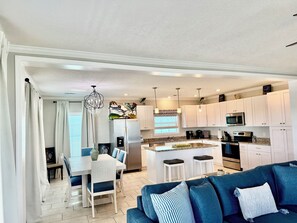 A modern kitchen with white cabinets, a stainless steel refrigerator, and a dining area with a white table and blue chairs.