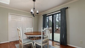 A dining room with a round wooden table, four chairs, a chandelier, a sliding glass door, and a view of the outdoors. - Pinehurst No. 6 Golf Front Getaway (Pinehurst)
