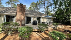 A single-story house with a brick chimney, a covered patio with outdoor furniture, and a lawn with small shrubs. - Pinehurst No. 6 Golf Front Getaway (Pinehurst)