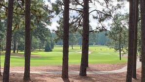 A view of a golf course with tall pine trees in the foreground and a clear path leading to the green. - Pinehurst No. 6 Golf Front Getaway (Pinehurst)