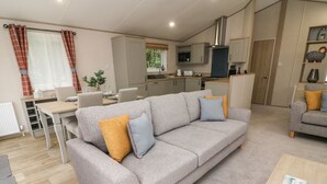 Una sala de estar moderna con un sofá gris, dos cojines, una mesa de centro de madera y un comedor con mesa y sillas.
