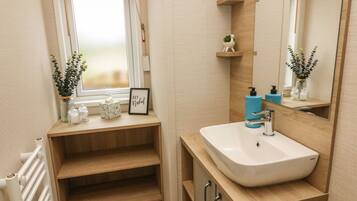 A modern bathroom with a large window, wooden shelves, a white sink, and a mirror.