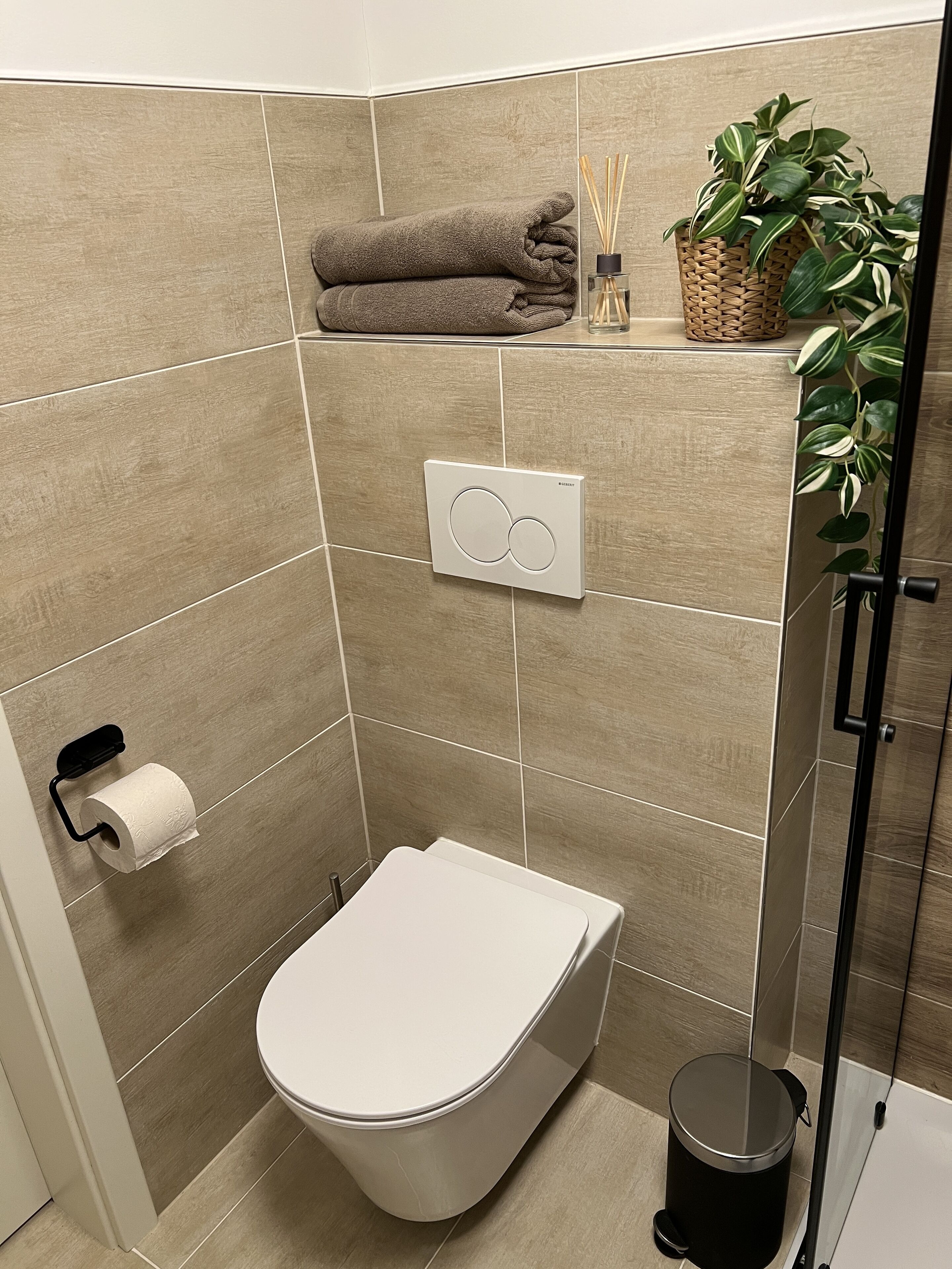 A modern bathroom with a toilet, a hand dryer, a trash bin, and a shower area.