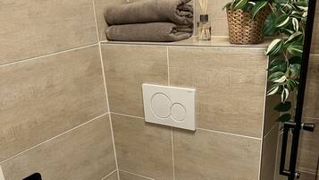 A modern bathroom with a toilet, a hand dryer, a trash bin, and a shower area.