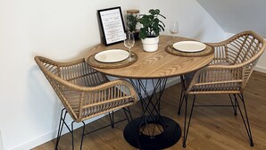 A dining area with a round wooden table, four wicker chairs, a potted plant, and framed artwork on the wall. - Sweet Spot | Studio apartment close to the city center (Trierweiler)