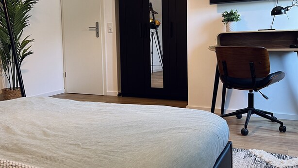 A bedroom with a bed, a desk, a chair, a TV, and a door leading to another room. - Sweet Spot | Studio apartment close to the city center (Trierweiler)