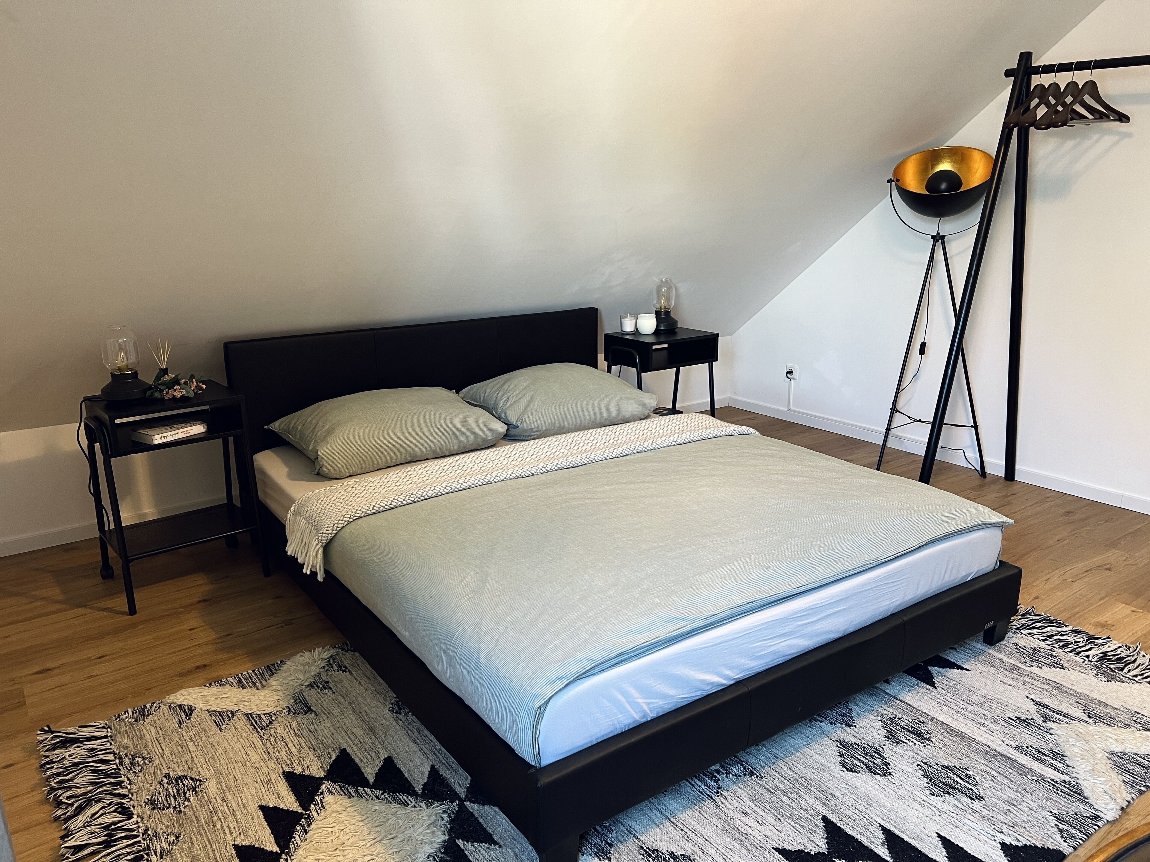 A modern bedroom with a bed, a nightstand, a lamp, and a hanging light fixture.