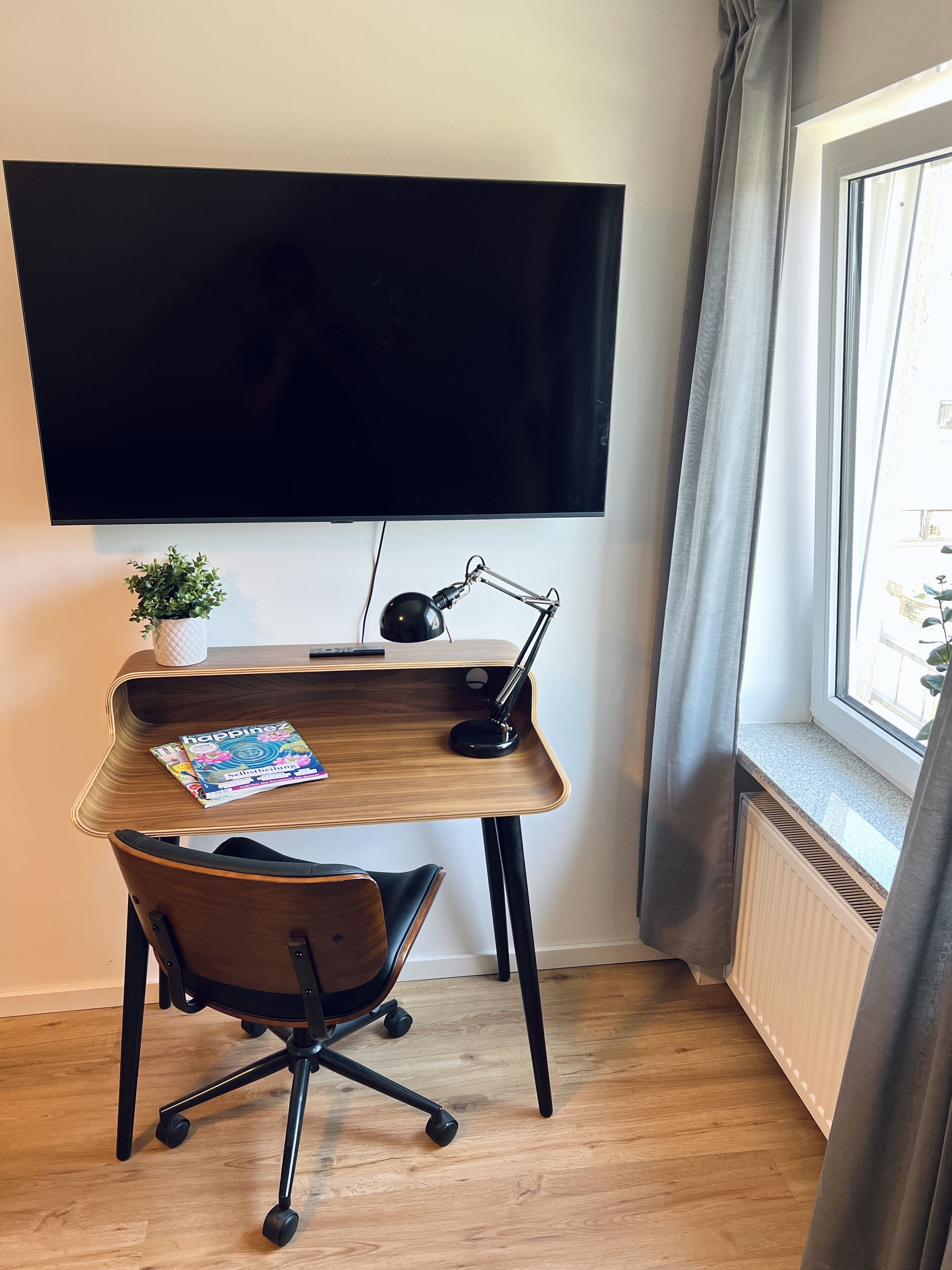 Een moderne kantoorruimte met een bureau, stoel, televisie en een raam met gordijnen.