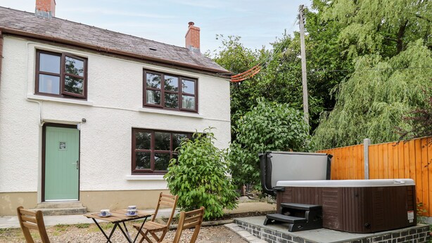 A two-story house with a patio area featuring a hot tub, wooden chairs, and a table. - Fisherman's Cottage (Llandysul)