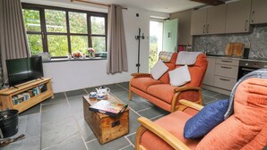 A cozy living room with a television, a wooden coffee table with a board game, a sofa with cushions, and a window with curtains. - Fisherman's Cottage (Llandysul)