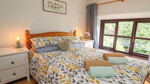 A bedroom with a wooden headboard, a bed with patterned bedding, two bedside tables with lamps, a window with curtains, and a framed picture on the wall. - Fisherman's Cottage (Llandysul)