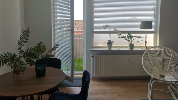 Ett rum med ett matbord, stolar, ett element och ett fönster med persienner.