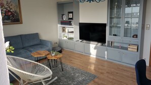 Ett modernt vardagsrum med en grå soffa, en vit fåtölj, en tv och ett blått skåp med glasdörrar.