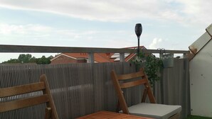En uteplats med trämöbler, inklusive ett bord och två stolar, placerad intill ett staket av korrugerad metall.