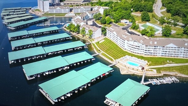 En vy från ovan över ett hotell vid vattnet, med flera båtar förtöjda, en stor byggnad med en swimmingpool och frodig grönska som omger området.
