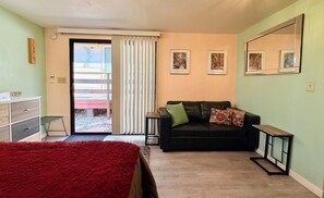 Una habitación con una cama, un sofá negro con cojines, una mesita y un espejo en la pared.