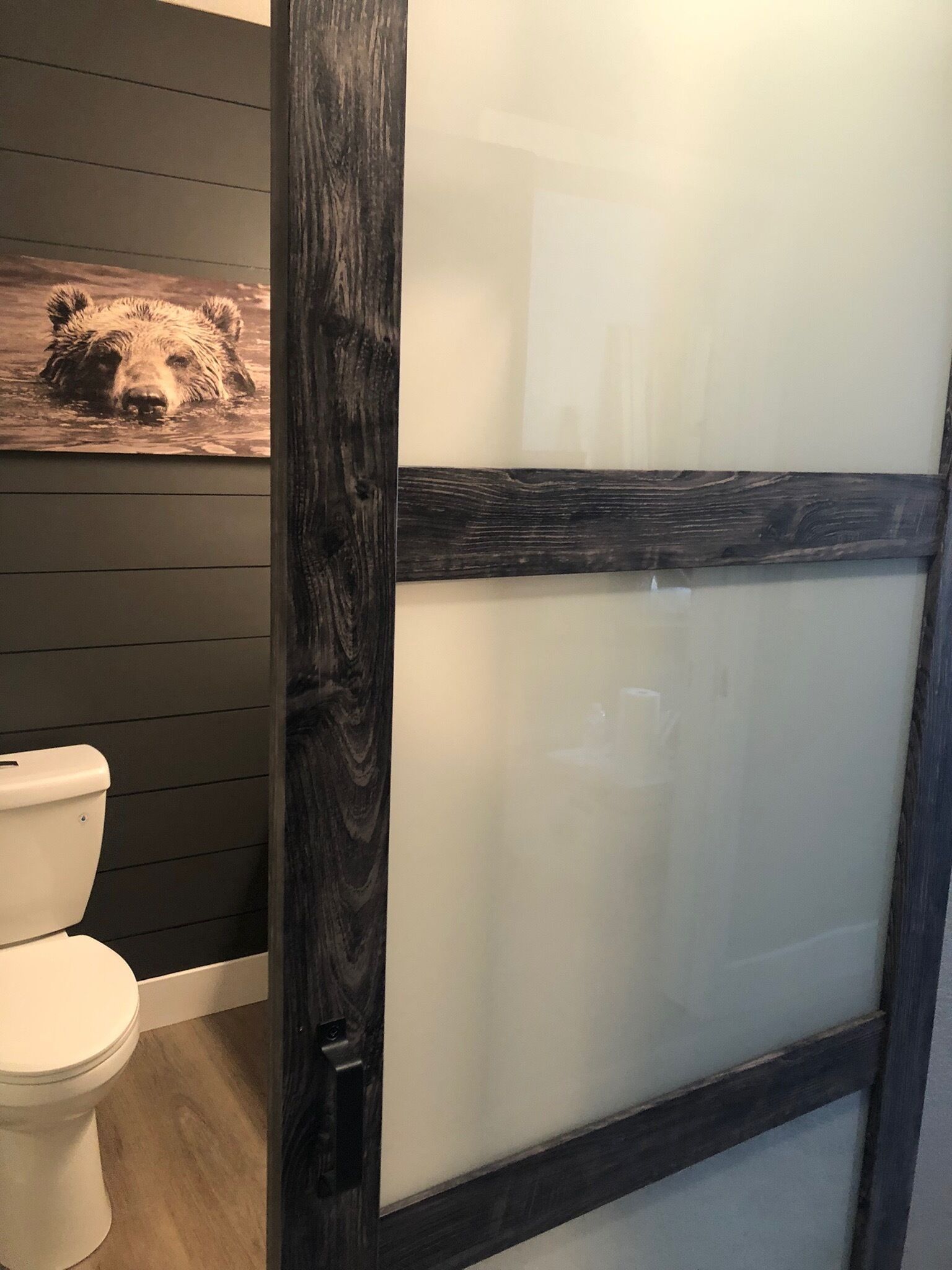 A bathroom with a white toilet, a wooden wall, and a glass shower enclosure.
