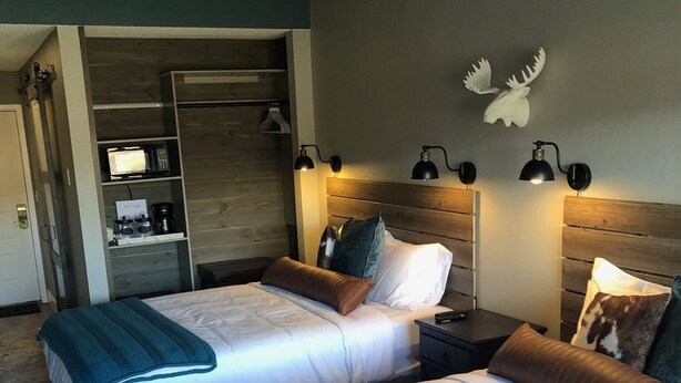 Une chambre d’hôtel avec deux lits, une armoire, un bureau et une lampe fixée au mur.