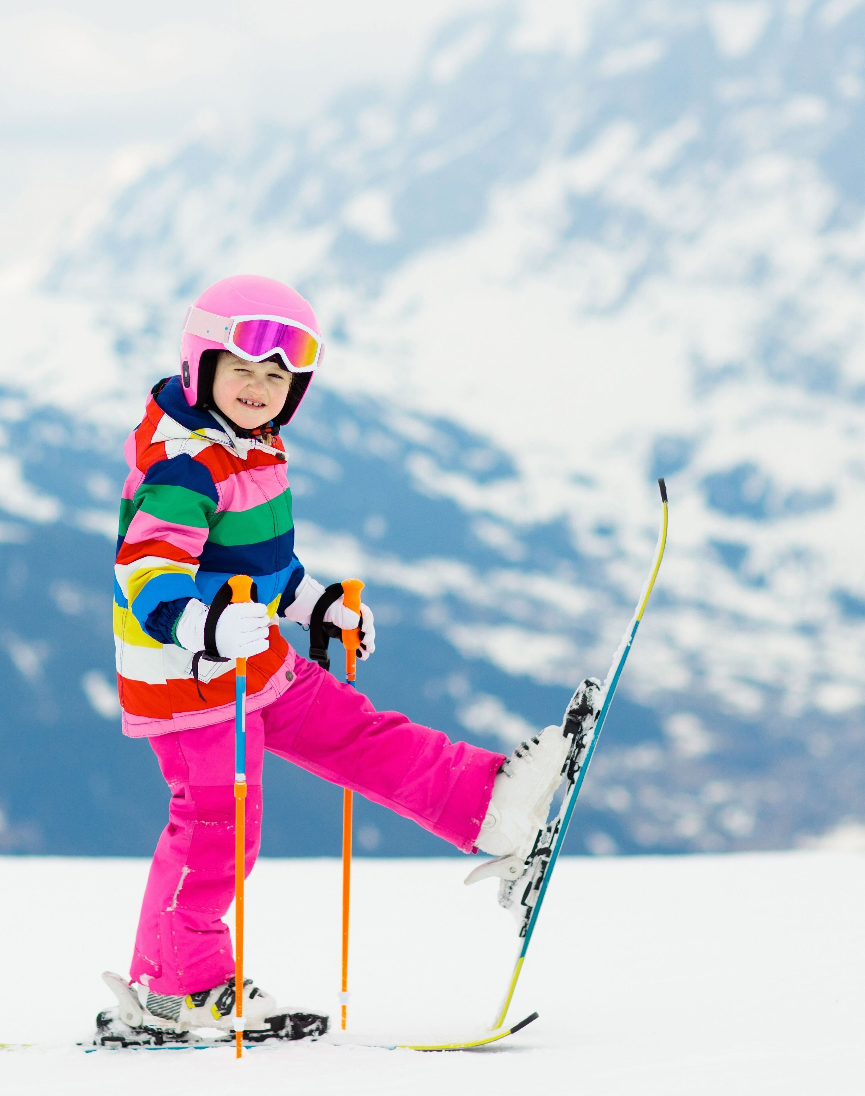 Een kind skiënd op een besneeuwde helling, met een kleurrijk jack en een roze helm.