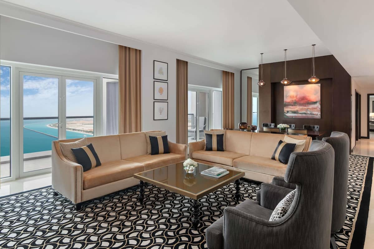 A modern living room with a sofa, armchairs, a coffee table, and a large window with a view of the sea.