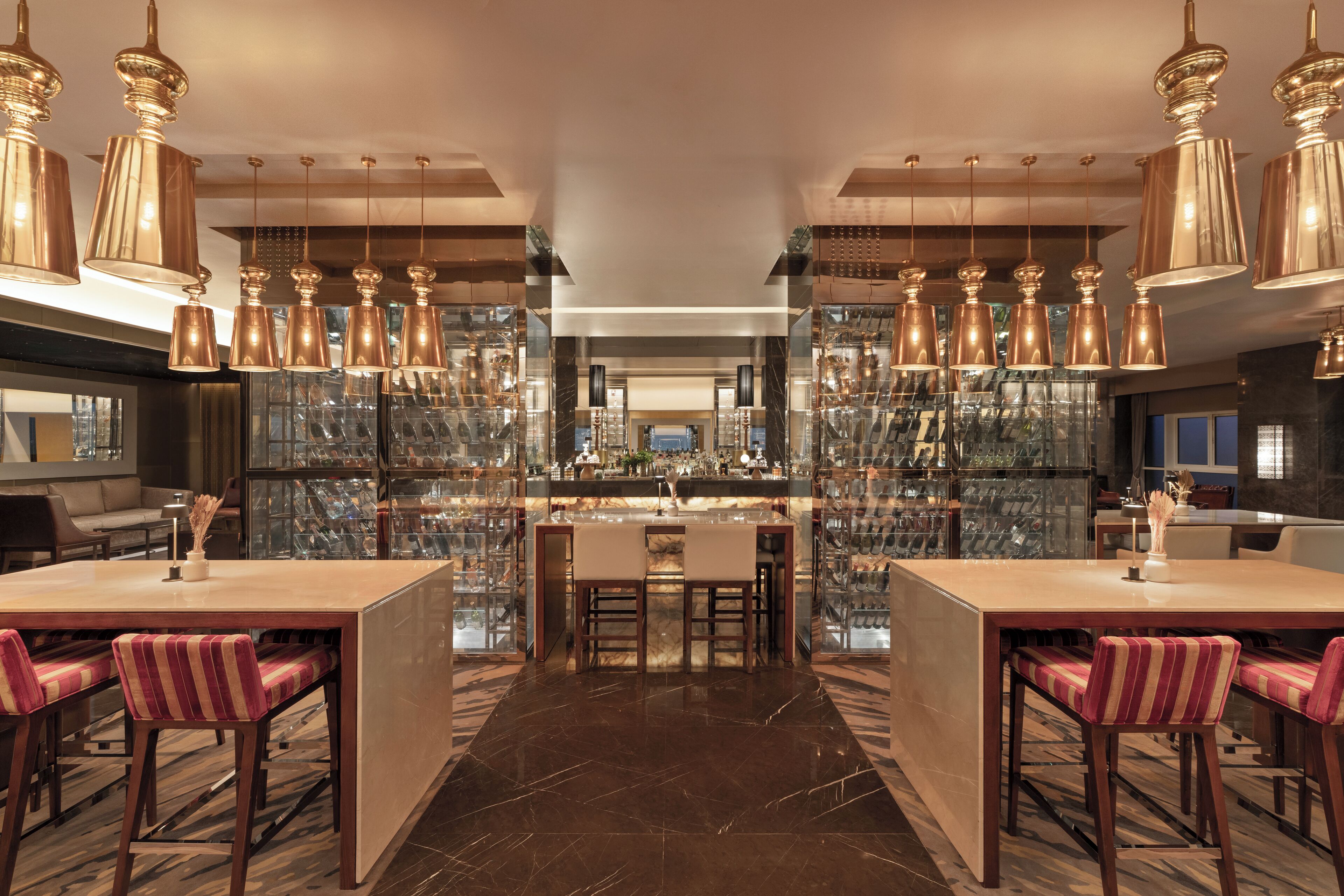 A modern bar area with multiple seating options, a central bar counter, and a display of various bottles and glasses.