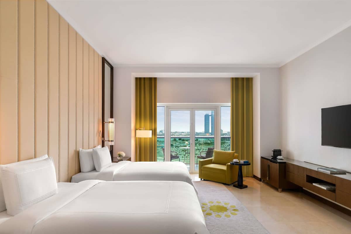A hotel room with two beds, a TV, a desk, and a view of a cityscape.