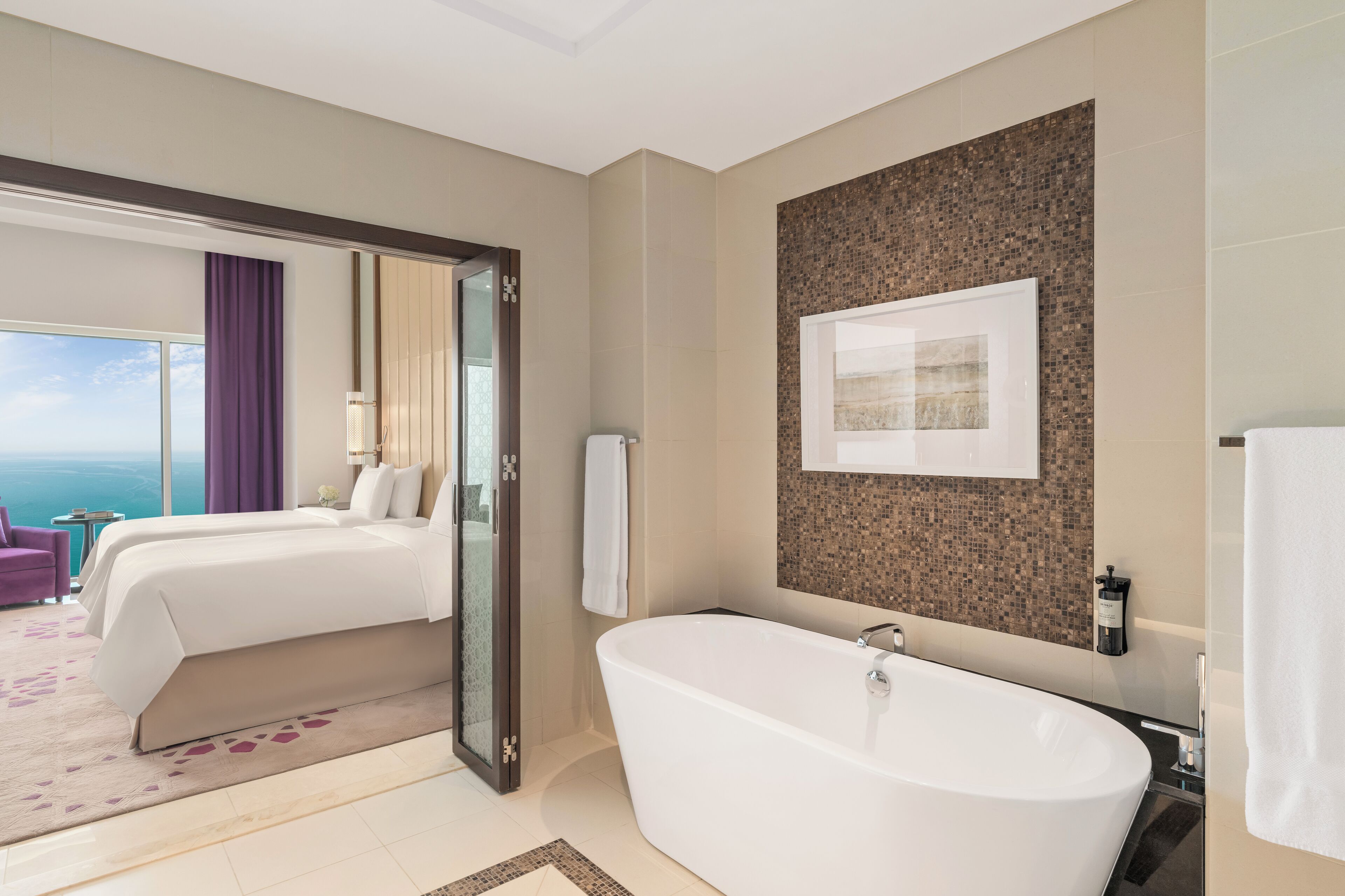 A modern hotel room with a large bed, a bathtub, and a view of the ocean.