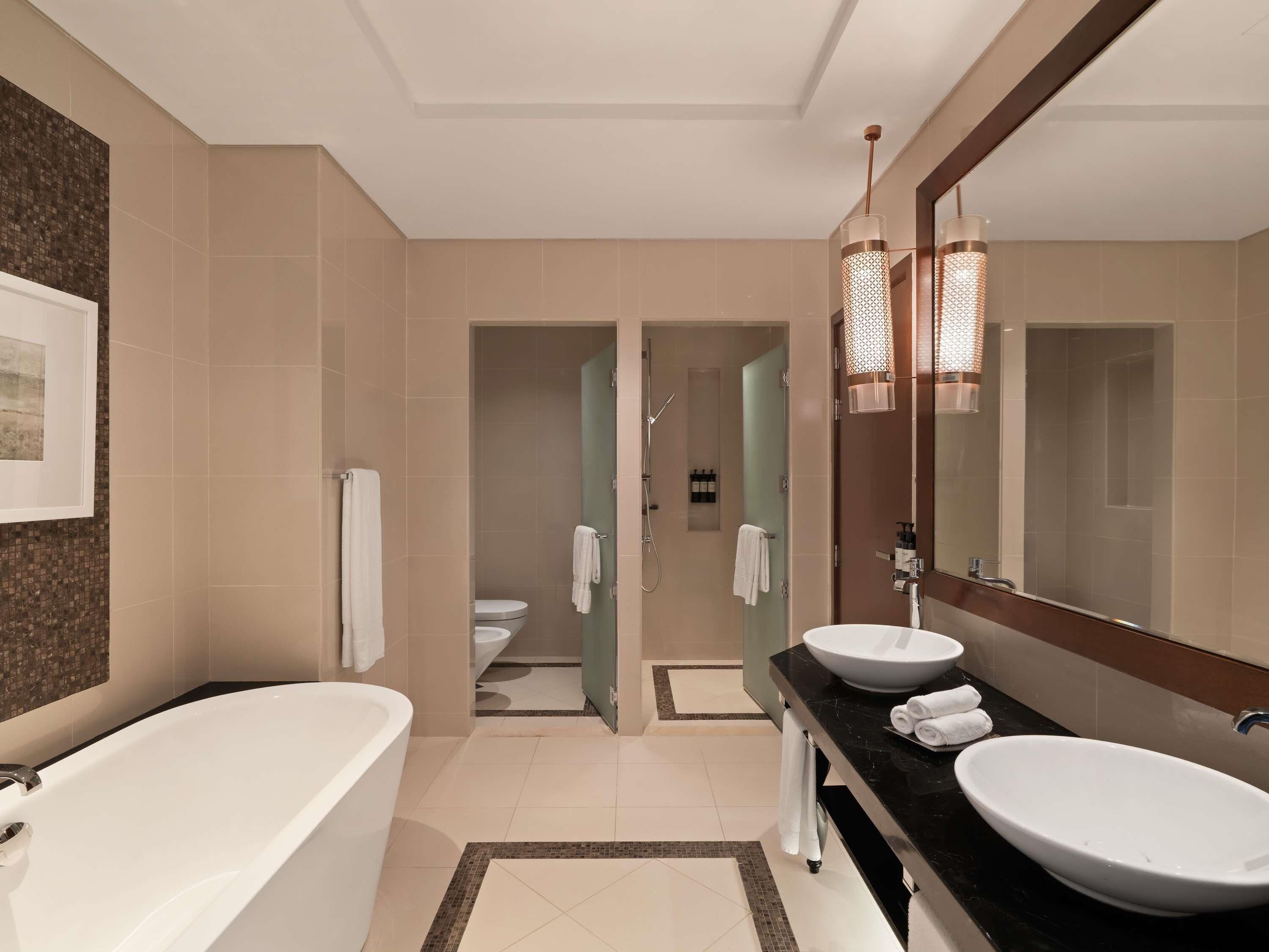 Une salle de bain moderne avec une baignoire, deux lavabos, un grand miroir et un espace douche.