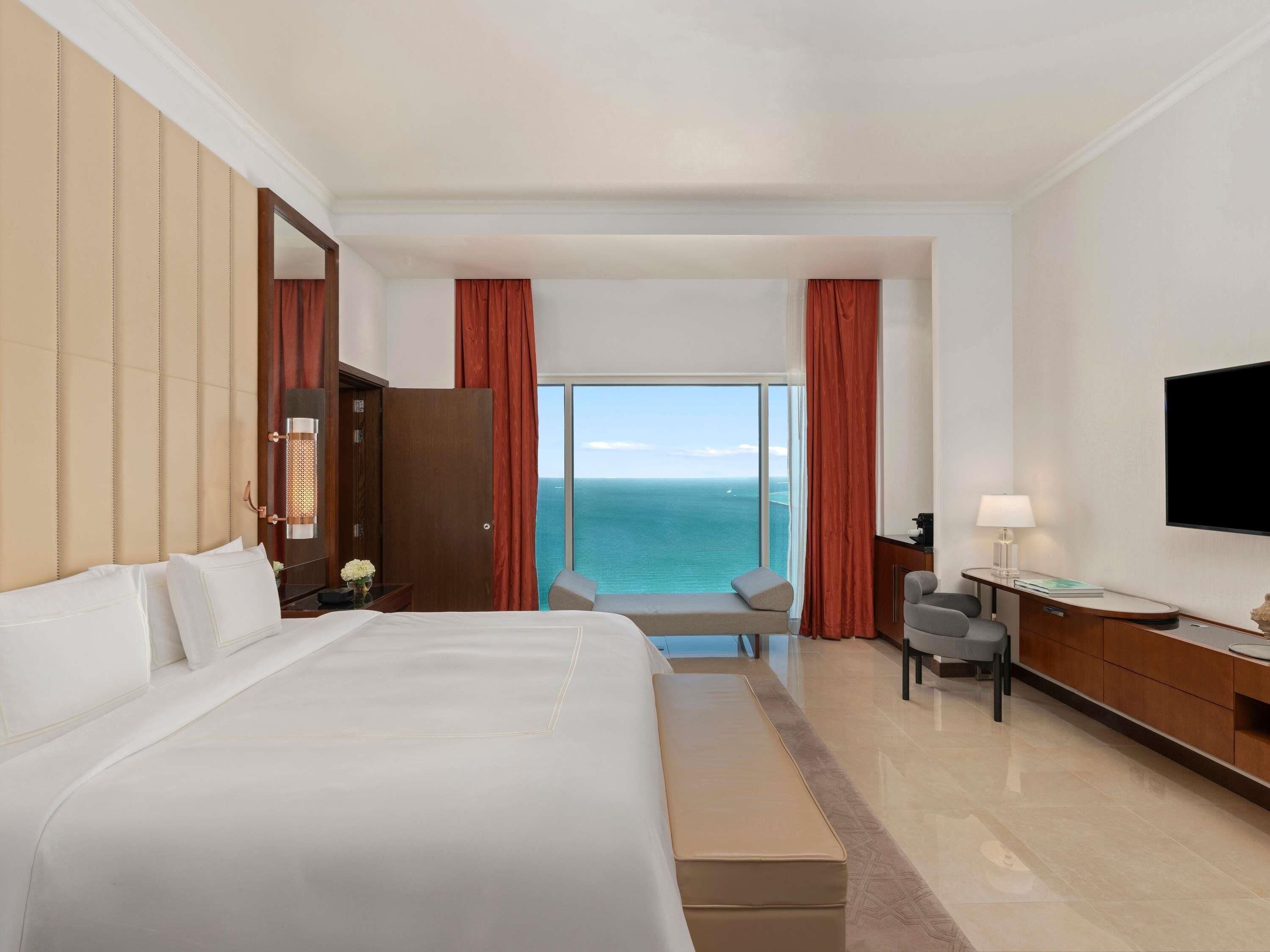 Ein Hotelzimmer mit Bett, Schreibtisch, Stuhl, Fernseher und Meerblick.
