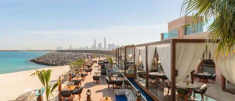 A rooftop bar with outdoor seating overlooking a beach and city skyline.