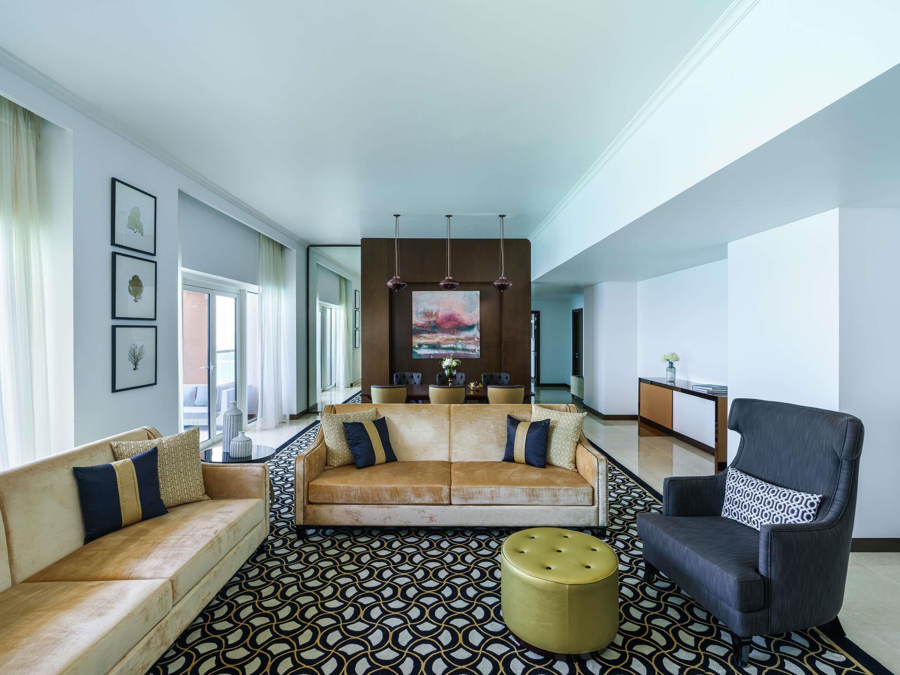A spacious living area with a sofa, armchair, ottoman, and a dining area in the background.